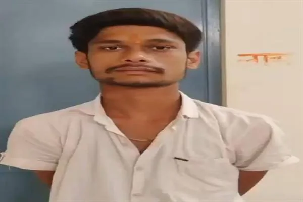 सफेद शर्ट पहने एक युवक कमरे के भीतर नीले दरवाजे के सामने खड़ा होकर कैमरे की ओर देख रहा है।