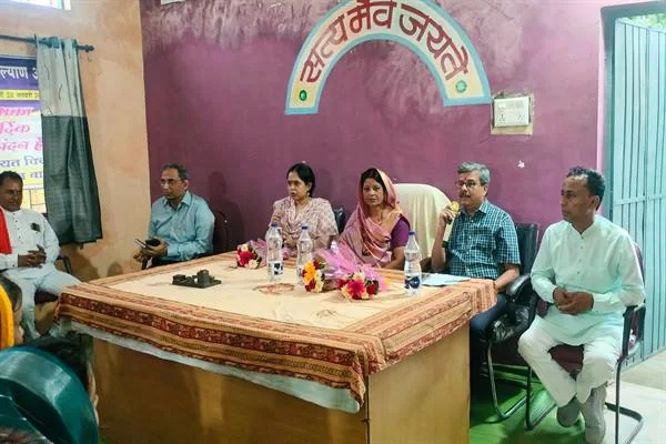 ग्राम पंचायत भवन के भीतर मेज के पीछे बैठे अधिकारी और जनप्रतिनिधि, दीवार पर 'सत्यमेव जयते' लिखा है और मेज पर पानी की बोतलें तथा पुष्पगुच्छ रखे हैं।